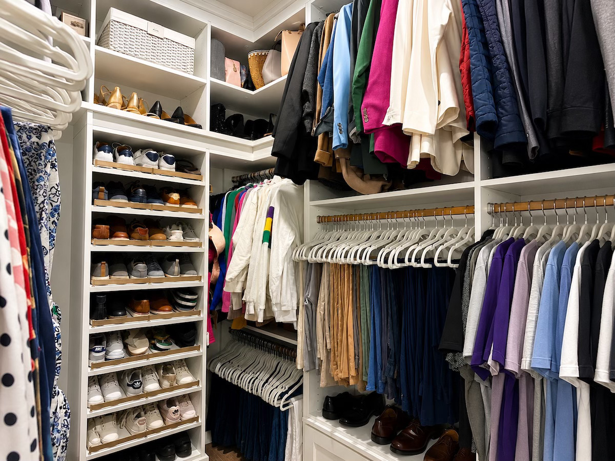 Organized walk-in closet with shoe shelves and color-sorted hanging clothes by Nola Organizers