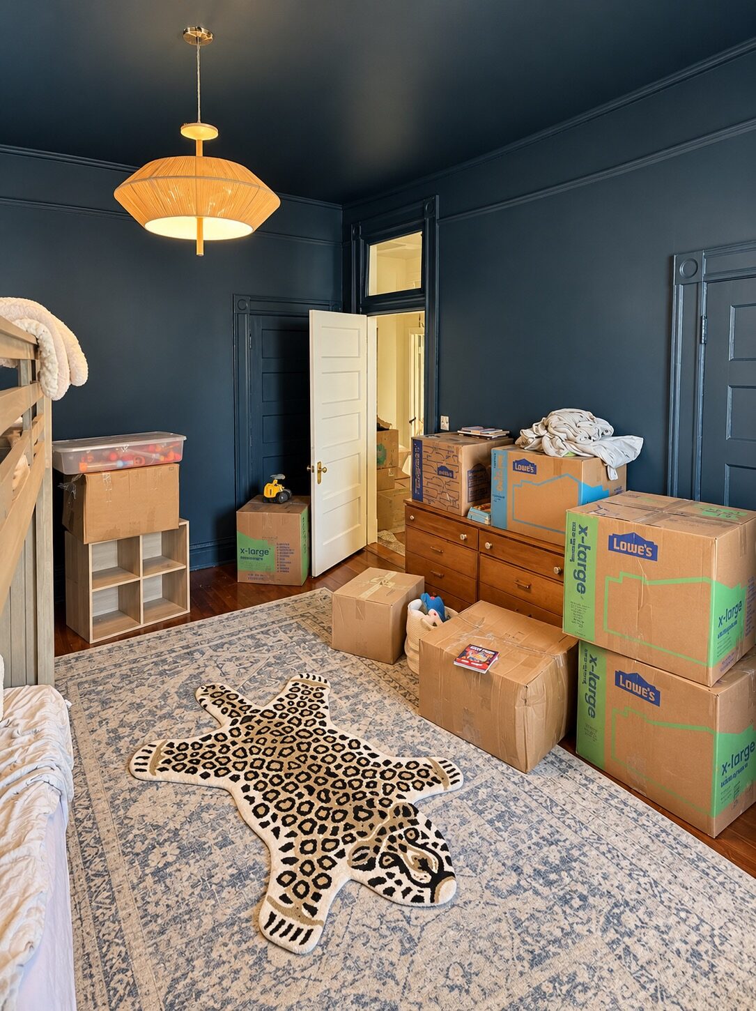 Navy children’s bedroom before unpacking, with moving boxes on the floor and dresser