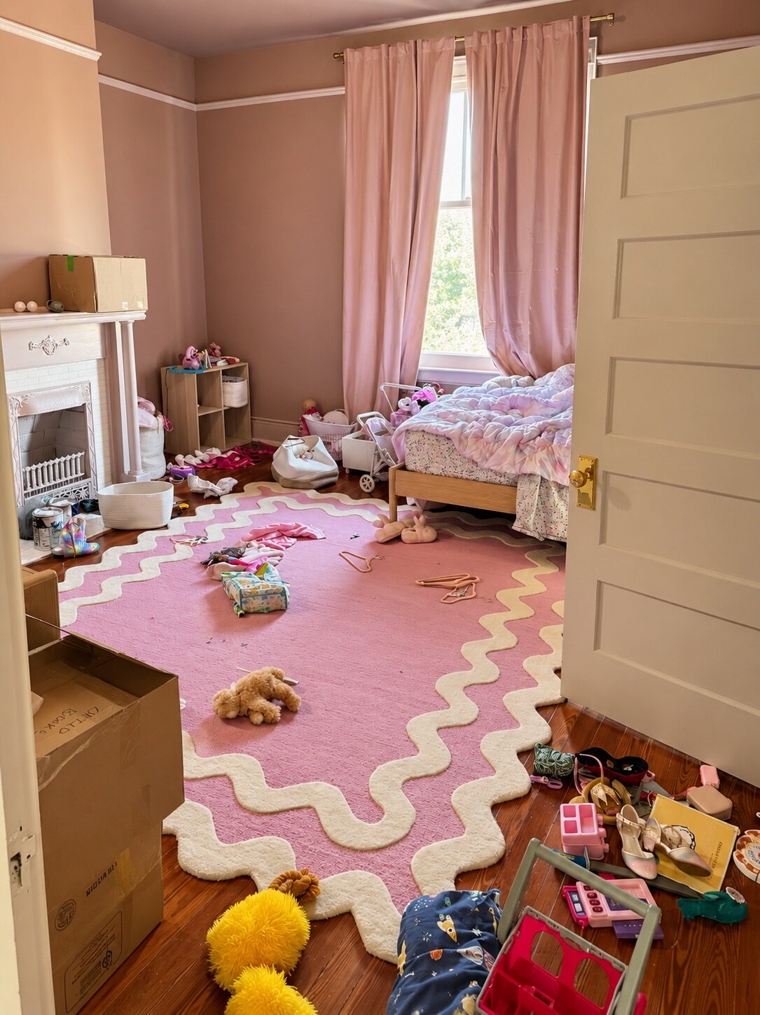 Pink children’s bedroom before unpacking, with boxes, toys, clothing, and hangers on the floor