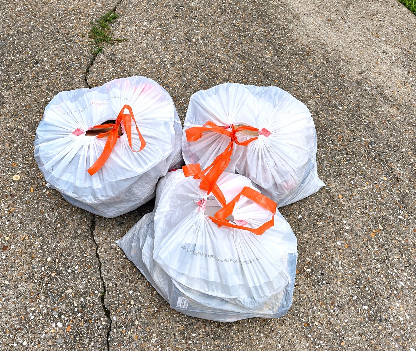 Three white bags with orange ties containing trash from the closet decluttering session