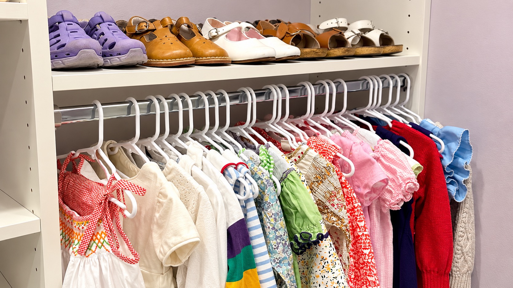 Closet with colorful children’s outfits hanging below a shelf of organized shoes