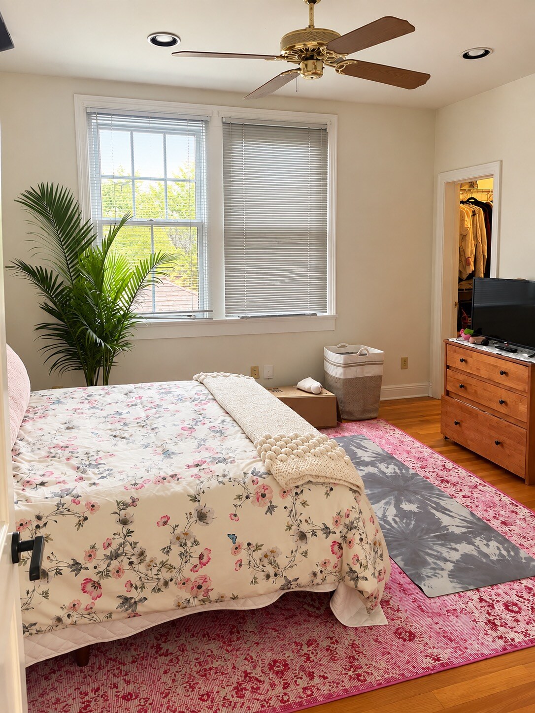 Bright bedroom with floral bedding, a wooden dresser, and a neatly arranged closet.